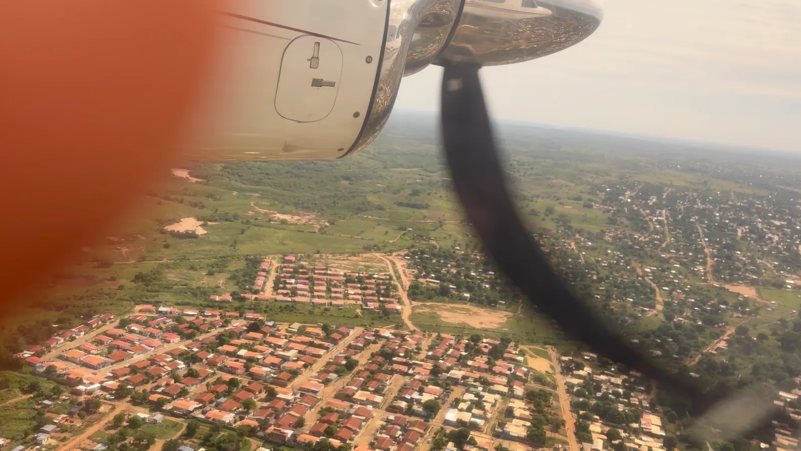 A view of fields and a town through an aircraft window, with the engine and propeller visible.