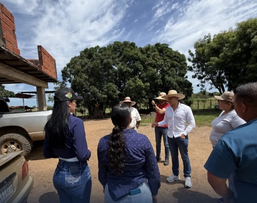 A group gathers outdoors beside farm vehicles for a conversation.