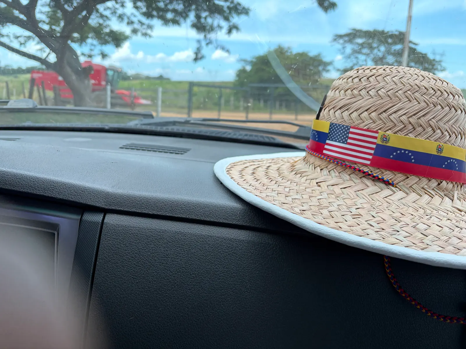 A straw hat with Venezuelan and U.S. flags rests on a vehicle dashboard.