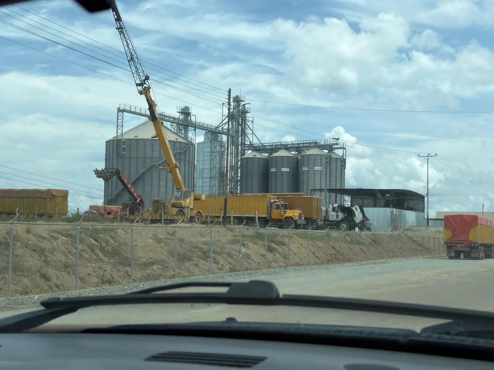 Grain silos, trucks, and a crane viewed from the road.